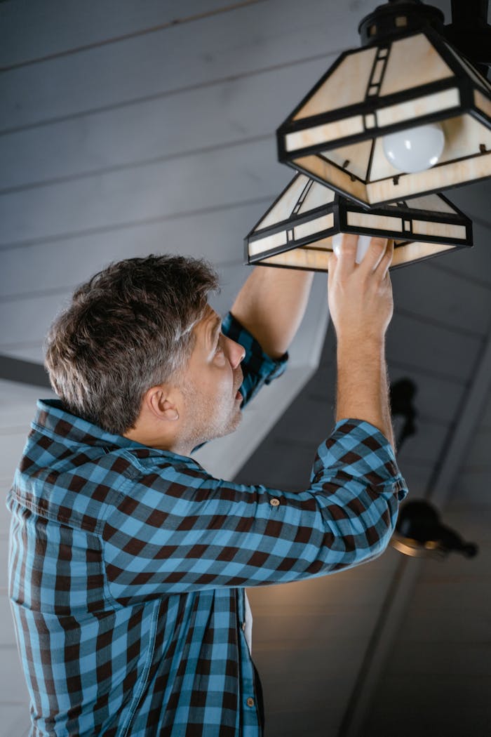 about-01 Adult male fixing pendant light indoors, wearing plaid long sleeves. Home maintenance scene.